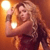 A pixelated figure with long curly hair holds a glowing object against a warm orange background.