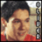 Pixelated image of a person with dark hair wearing a red top, holding a white object near their face against a blurred background.