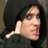 Pixelated static image of a person with long dark hair wearing a dark hooded garment, holding a white object near their face.
