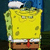 Yellow cartoon character with green spots, white collar, brown pants, red tie, and blue hat stands against dark background.