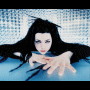 A woman with long black hair and blue eyes reaches forward from a light blue background, her expression neutral.