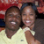 Two people in close proximity, one wearing a light-colored shirt and the other dark clothing, against a blurred red background.