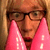 Pixelated image of a person with light brown hair and glasses holding pink objects near their face, next to purple text on black background.