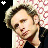 Pixelated portrait of a person with light brown hair and dark eyes, wearing a black top against patterned background.