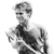 Pixelated grayscale image of a person with short hair holding a dark object, wearing a light shirt with a patterned design.