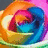 A pixelated abstract composition with swirling orange, blue, pink, and yellow hues forming a circular shape against a dark gray background.
