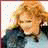 Pixelated static image of a person with light brown curly hair wearing dark clothing against a white background with scattered pastel squares.