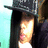 Pixelated image of a person wearing dark clothing and a cap, with light-colored hair visible beneath the cap against a gradient background.
