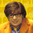 Pixelated static image of a person with brown hair wearing glasses and an orange jacket over a blue shirt against a yellow background.