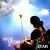 A person with dark hair tied back sits facing a bright star-like object against a blue sky with clouds and floating yellow shapes.