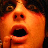 Pixelated orange-toned face with wide open mouth and dark eyes against a black background.