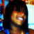 A person with dark hair and bangs smiles broadly in a pixelated image with blue and red background elements.