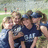 Group of people in sports uniforms embracing outdoors with 'softball!' text on a black banner.