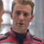 Static 64x64 pixel icon showing a close-up of a person in a red and black jacket against a blurred background with light reflections.