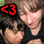 Two people in black shirts pose together with a heart symbol changing color from red to green to blue.