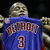 Pixelated figure in blue jersey with red text and number, holding a basketball against dark background.