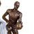 A static image shows a person with long brown hair and blue eyes, wearing a white shirt, alongside a bronze statue of a muscular figure holding a helmet.