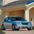 A blue sedan with silver accents is parked under a brown garage door, viewed from a low angle with a light-colored building facade in the background.