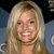 A static pixelated image of a person with long blonde hair smiling, wearing a light-colored top against a dark background with blue elements.