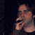 A person in a dark top holds a small dark object near their mouth across showing slight head and hand movement