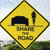 Yellow diamond-shaped road sign with black border showing a dark vehicle silhouette on a road, text below reads 'BUMPY ROAD', background has sky and greenery.