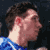 Pixelated static image of a person's profile with brown hair, blue clothing, and visible ear against dark background.