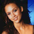 Pixelated close-up of a person with light skin tone, dark hair, and a smiling expression, wearing a dark top against a dark background with blue accents.