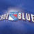 Blue background with a blue and white shield icon containing red triangle, next to partial text 'BLUE' in white block letters.