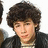A pixelated image of a person with curly brown hair wearing a dark jacket over a light shirt, with green text on a black background.
