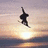 A pixelated silhouette of a figure in mid-air against a sunset sky with water below, rendered in low-resolution style.