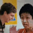 Two individuals with dark hair appear in a static image; one wears a white top, the other an orange garment against a yellow and light gray background.