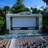 Pixelated static image of a building facade with a large rectangular window, greenery above, and a blue sky background.