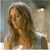 A pixelated image of a person with long brown hair wearing a white headband, seated in a softly lit indoor setting with a lamp visible in the background.