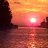 Sunset over water with silhouetted rock formations, transitioning from bright orange to pink hues across four