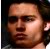 Pixelated close-up of a person's face with light brown skin tone, dark eyes, and dark hair against a dark background.