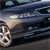 A static image of a dark-colored sedan with visible headlights and a front wheel, captured from a low angle on a paved surface.