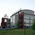 Pixelated static image of a large industrial structure with curved roof and vertical supports, set against a light sky and green ground.