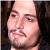 Pixelated close-up of a person's face with light skin tone, dark hair, and neutral expression against dark background.