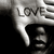 A hand with 'LOVE' written on the palm holds a small object, with a blurred face visible below.