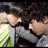 Pixelated image of two figures in close physical contact, one with light skin and dark hair, the other with light skin and brown hair, both wearing dark clothing.