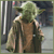 Pixelated image of a green-skinned humanoid figure with large ears wearing brown robes and holding a staff, standing against a dark background.