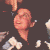 Pixelated image of a light-skinned figure with closed eyes and a neutral expression, surrounded by scattered white and light brown shapes on a dark brown background.