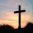 A static image with a blue background, featuring a black cross silhouette against a sunset sky on the left and pixelated text reading "We need you Miss you Abby V Love you!" in light blue.