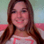 A pixelated portrait of a person with long brown hair wearing a white top with pink accents against a soft green and blue background.