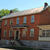 A static pixelated image of a two-story brick house with a light-colored roof, multiple windows, and a chimney under a clear blue sky.