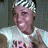 Pixelated image of a person wearing a white shirt with dark text and a checkered headband, set against a dark background.