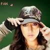 A person with long dark hair adjusts a camouflage-patterned cap with both hands against a solid green background.
