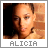 Pixelated close-up of a person with light skin tone, dark hair, and closed eyes, set against a brick wall background with text reading ALICIA below.