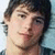 Pixelated close-up of a person with dark hair, light skin tone, and visible facial features including eyes, nose, mouth, and chin against a blurred background.