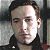 Pixelated close-up of a person with short dark hair wearing a dark jacket against a blurred background.